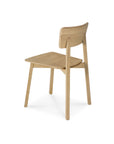 The Casale Dining Chair - Oak by Ethnicraft features a minimalist curved backrest and flat seat, crafted from European oak. The modern design reflects classic European refinement, displayed at an angle on a white background.