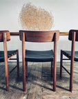 A SOBU Cesco Dining Chair - Walnut with a top grain leather seat sits at a wooden table. Behind it, dried tumbleweed adds visual interest, while two similar chairs are partially visible on either side.
