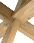 Close-up of Ethnicraft’s Circle Dining Table - Oak, highlighting the intersecting legs and elegant design. The natural grain of light European oak stands out against a white background.