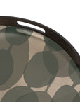 A close-up of the Ethnicraft Connected Dots Glass Tray - Round / Small, showcasing organic forms and a modern abstract leaf pattern in green and beige, with a convenient cut-out handle.