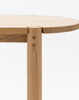 Close-up of the Wooden Stories Cove Dining Table - Light Oak, showcasing its rounded tabletop and vertical leg with visible wood grain and joinery, inspired by Sydney Harbor, set against a plain white background.