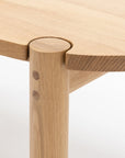 Close-up of the Wooden Stories Cove Dining Table - Light Oak, highlighting its seamless round leg joinery, visible wood grain, and wooden dowel details—an elegant choice to enhance your dining experience.