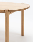 Close-up of the Wooden Stories Cove Dining Table - Light Oak, featuring a rounded edge and cylindrical legs inspired by Sydney Harbor, embodies modern minimalist design against a plain white background for an elevated dining experience.