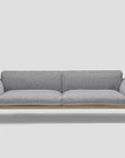 The Department Sofa 93" by Wooden Stories features modern gray fabric, Danish lines, a solid wood plinth, slim black metal legs, wide armrests, and a minimalist design—ideal for both commercial and domestic crossover spaces.