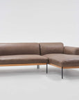 The Department Modular Sofa | Leather • M1 by Wooden Stories is a modern sectional with brown leather, a solid wood base, slim black metal legs, and a right-side chaise lounge, inspired by Danish collections and shown on a plain white background.