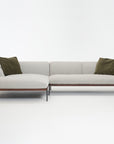 The Department Modular Sofa | Fabric • M4 by Wooden Stories features a modern light gray L-shape, slim black legs, and two olive green throw pillows, inspired by Danish collections and shown against a white background.