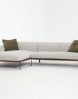 The Department Modular Sofa | Fabric • M4 by Wooden Stories is a modern light gray L-shaped sectional with sleek black legs, an FSC-certified oak trim base, and two olive green pillows, displayed against a plain white background.