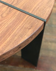 Close-up of the SOBU Dial Coffee Table - Walnut, featuring eastern walnut with a smooth, rounded edge and contrasting dark metal leg, shown on a matching wooden floor.