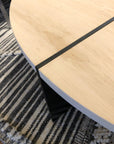 A close-up of the SOBU Dial Coffee Table - White Ash features a solid ash top with a light finish and black metal legs, placed on a textured rug with striped and braided gray, white, and black patterns.
