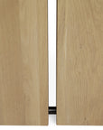 Close-up of two solid oak panels from the Ethnicraft Double Extendable Dining Table, showing a narrow gap that highlights the natural wood grain and a small section of a dark horizontal rod at the bottom.