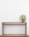 The Emily Console - Oak by SOBU stands against a white wall, with a potted spider plant placed on the top right corner of this minimalist furniture piece.