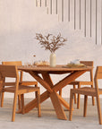 An Ethnicraft teak table with four EX1 Outdoor Dining Chairs sits by the stairs, set with plates, glasses, bread, and a decorative vase. A potted tree adds greenery to this inviting outdoor scene.