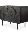 The Ethnicraft Graphic Dresser is a modern black solid teak piece with three drawers, featuring an abstract geometric carved front and slender straight metal legs.