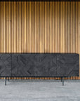 The Ethnicraft Graphic Sideboard - 4 door features modern geometric patterns in solid black teak, standing on a gray tile floor against vertical wooden slats—crafted to contract grade quality.