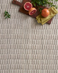 A wooden board with grapefruit, green leaves, and a yellow napkin rests on the Loloi Hadley Rug - Oatmeal, a textured beige geometric hand-cut carpet.