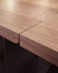 Close-up of the SOBU Hinge Extension Dining Table in black walnut, featuring a modular interlocking design with visible seams, a smooth light brown finish, and a silver screw on the edge.
