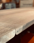 Close-up of the SOBU Hinge Extension Dining Table - White Oak, highlighting its solid wood grain, texture, and visible screw in the corner. The background is elegantly blurred for emphasis on craftsmanship.