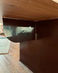 A view from under a wooden desk shows a dark, curved privacy panel attached, with a textured rug and wood floor behind—crafted to complement the SOBU Hinge Extension Dining Table - White Oak or any customizable table.