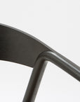 Close-up of the Inlay Dining Chair by Wooden Stories, showcasing black oak, a curved plywood backrest, solid wood arms, and a leather seat against a plain white background.
