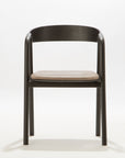 The Inlay Dining Chair by Wooden Stories features a black oak frame, rounded plywood backrest, and light leather seat, displayed against a plain white background.
