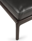 Close-up of a dark brown mahogany varnished leg with a smooth, rounded corner, supporting a black leather cushion with visible stitching—an elegant detail from the Ethnicraft Jack Footstool - Black Leather.