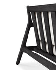 Close-up of the back corner of the Ethnicraft Jack Outdoor 3 Seater Sofa in black teak with vertical slats and angled legs, partially revealing its off-white cushion against a plain white background.