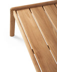 A close-up of the Ethnicraft Jack Outdoor Coffee Table - Teak showcases its minimalist design, smooth Grade A teak, clean lines, angled legs, and horizontal slats, focusing on one corner of the table.