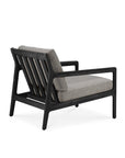 The Jack Outdoor Lounge Chair by Ethnicraft features a black teak frame, angled legs, slatted backrest, and thick mocha cushions—making it a stylish and comfortable choice for any outdoor lounge.