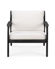 The Ethnicraft Jack Outdoor Lounge Chair features a black teak frame with thick off-white cushions, shown from the front on a white background. This modern armchair is ideal for elegant indoor or outdoor lounge spaces.