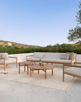 The Jack Outdoor Lounge Chair by Ethnicraft features teak wood and off-white cushions, shown as part of a modern outdoor setting with matching pieces, arranged on a light rug in a tranquil natural landscape.
