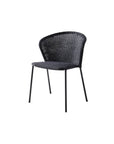The Lean Chair - Black by Cane-line features black Cane-line Weave rattan, a rounded backrest, and four slender metal legs, shown against a plain white background.