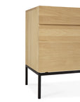 A close-up of the Ethnicraft Ligna Sideboard - 2 door shows its modern European oak build with a natural finish, clean lines, and black metal legs—only one side and part of the front are visible.