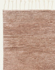 A close-up of the Malawi Rug - Blush by Armadillo&Co displays its artisanal feel with a textured, light brown hand-knotted design, horizontal lines, and cream-colored tassels along the top edge.