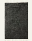 The Malawi Rug - Kelp by Armadillo&Co is a rectangular dark gray woven rug with subtle horizontal lines and fringed tassels on the top and bottom, shown against a light background.