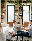 A man and two boys play in a bright living room with white couches and green plants. The SOBU Mars Live Edge Bench - Black Ash stands out, showcasing its natural wood beauty in the cheerful space.