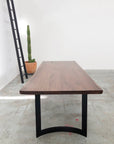 The SOBU DZ TRIAL Mars Live Edge Dining Table with black metal legs is centered in a minimalist room with a concrete floor, accompanied by a tall potted cactus and a black ladder against a plain white wall.