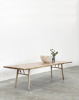 The SOBU Mars Live Edge Dining Table in white ash with wood legs sits on a concrete floor. A light bowl and dark vase with greenery rest on it beneath a plain white wall.