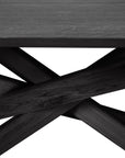 Close-up of the dark European oak legs on Ethnicrafts Mikado Dining Table Oval - Black Oak, intersecting in a crisscross pattern under the tabletop, with a white background emphasizing the woods rich texture and structure.