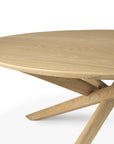 A close-up of the Ethnicraft Mikado Coffee Table Round - Oak, featuring solid oak construction with a smooth top and intersecting angled legs, displayed against a plain white background.