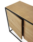 The Ethnicraft Monolit Sideboard - 2 door features a minimalist design with solid oak, a black metal frame, and partially open doors that reveal storage, showcasing the brand’s signature modern style.