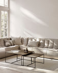 A bright, minimalist living room showcases the Ethnicraft N701 Sectional Sofa in beige, accented by neutral pillows and modern nesting tables, with sunlight streaming onto a light rug for a timeless European look.