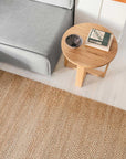 Minimalist living room with a light gray sofa, round wooden coffee table holding a dish and two books, set on the Armadillo&Co Nest Rug in Natural atop a white floor.