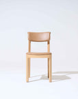 The Wooden Stories Noki Dining Chair features light oak and a curved tan leather seat and backrest. It is set against a plain white background with a faint shadow on the right.