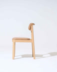 The Noki Dining Chair | Light Oak with Leather by Wooden Stories is a contract grade solid wood chair with light brown leather cushioning on the seat and back, shown in profile against a plain light background, casting a faint shadow to the right.
