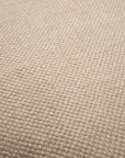 Close-up of a beige textured fabric with a grid-like pattern. The Nomad Outdoor Rug by Ethnicraft is crafted from recycled PET yarns, featuring tightly woven threads for a uniform, slightly raised surface suitable for indoor or outdoor use.