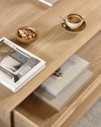 The Ethnicraft Nordic Coffee Table - Oak displays a cup of espresso on a saucer with a spoon, a bowl of mixed nuts, and several art books—some arranged on top, others placed on the lower shelf.