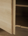 A close-up of the Ethnicraft Nordic Sideboard - 2 door shows its solid oak grain, a slightly open door, and an unfinished interior shelf.