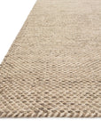Close-up of the Loloi Oakwood Rug - Wheat, highlighting its beige handwoven wool texture and thick, rounded edges. The rug extends toward the upper right corner against a white background.