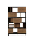The Ethnicraft Oscar Rack - Teak is a modern bookshelf with a black frame, asymmetrical compartments, and a mix of open and closed storage in solid natural teak, shown against a white background.