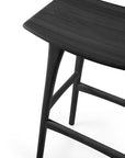 Close-up of the Osso Barstool - Black by Ethnicraft, made from black-stained solid oak with a smooth dark finish, highlighting part of the seat and upper legs against a white background.